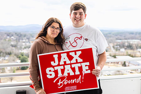 A freshman prospect and his mom hold the Jax State Bound sign on top of the library