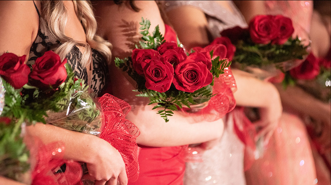A row of homecoming showcase beauties, holding their rose bouquets