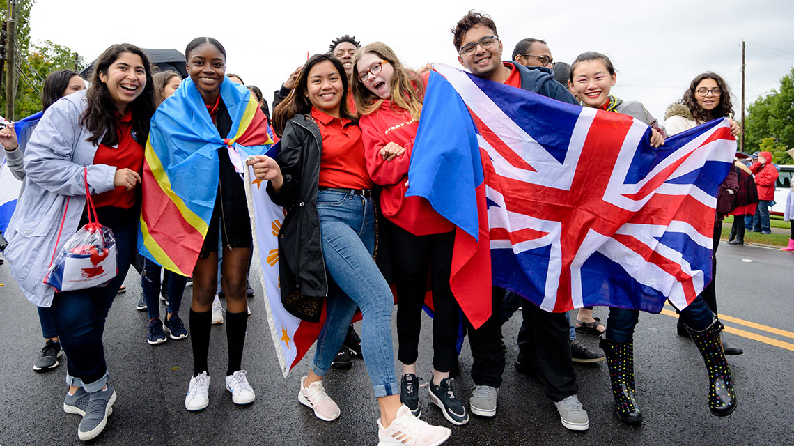 International students, draped in the flags of their nations, marching in the Homecoming parade