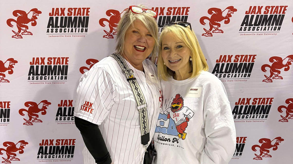 Alumnae posing in front of a Jax State photo backdrop