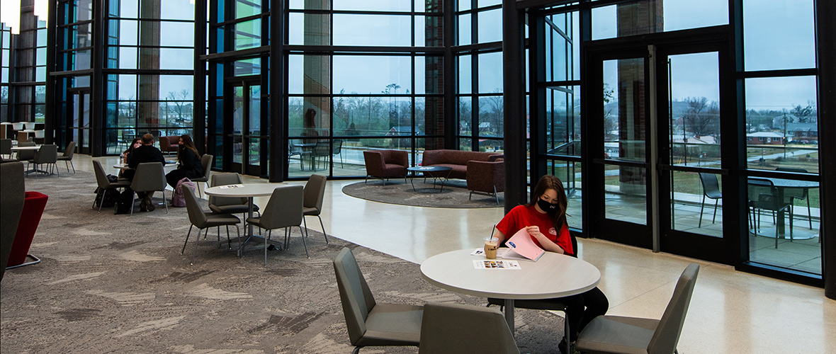 A female student works at a table in the front atrium of the Merrill Hall