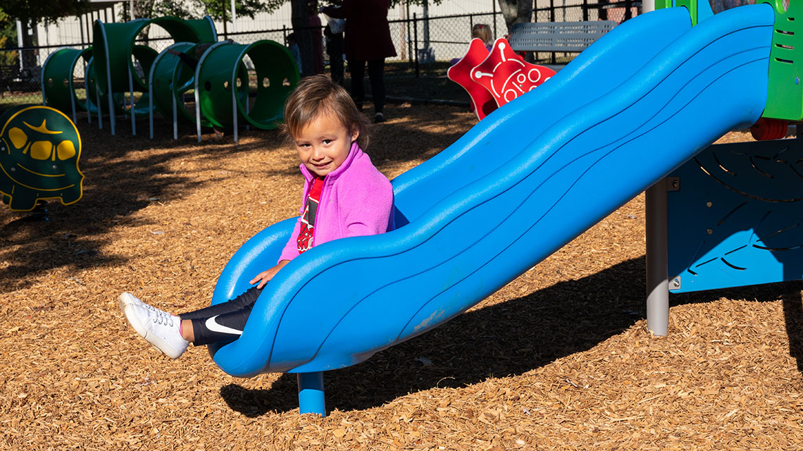 A little girl slides down the slide on the playground