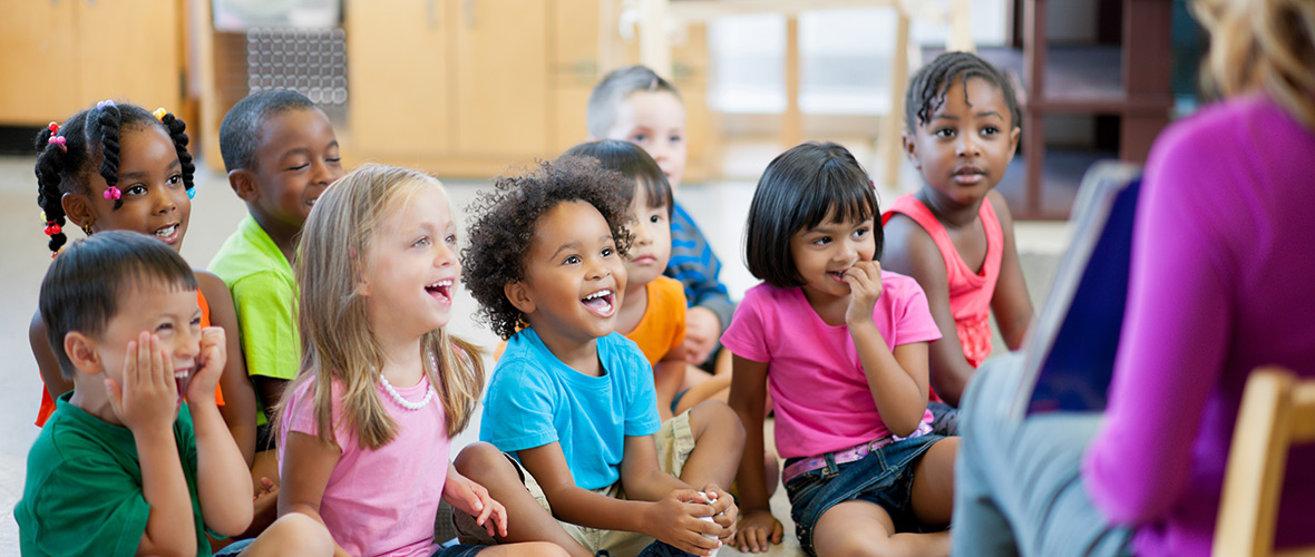 Young children sitting while listening to teacher read a book