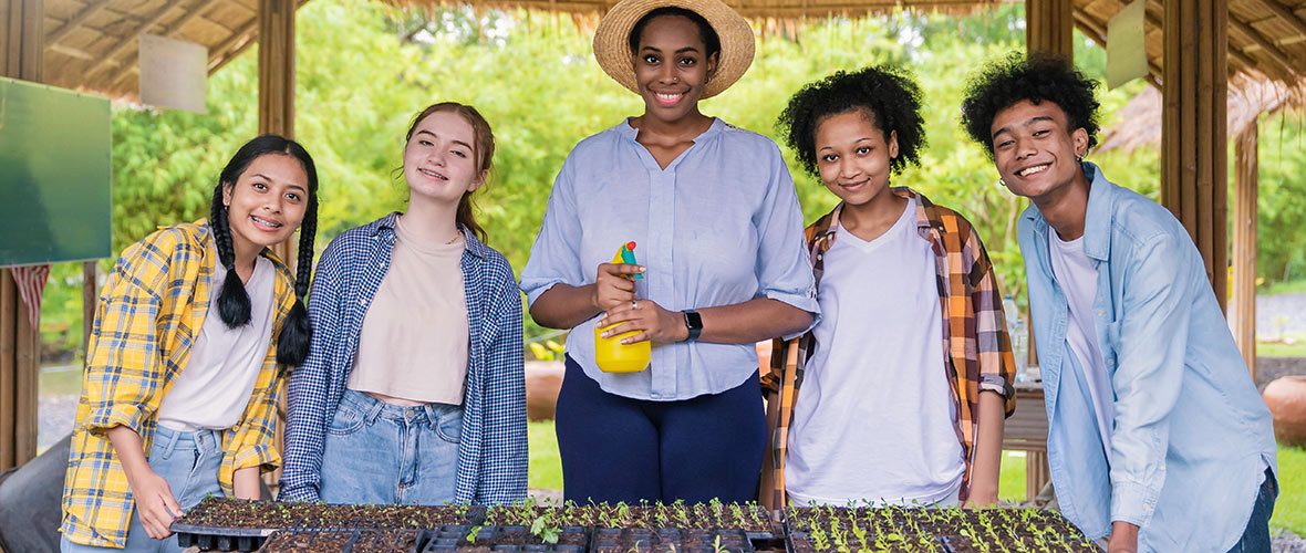 A female teacher shows teens how to grow seedlings in an outdoor classroom.