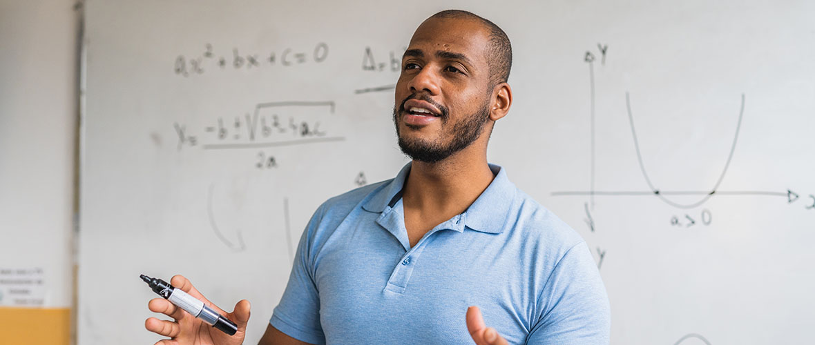 A math teacher lectures from in front of his whiteboard