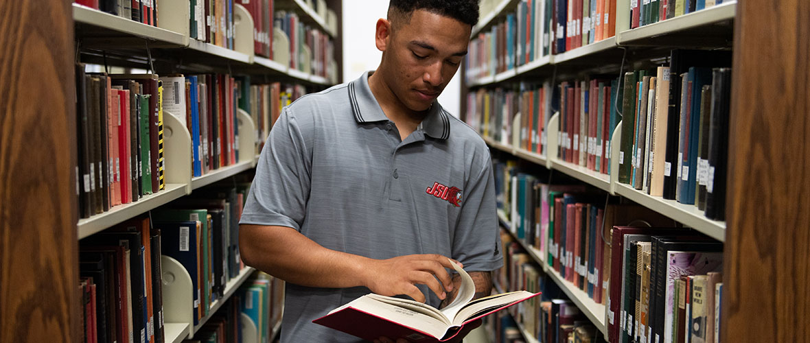 Student reading a book while standing in the library