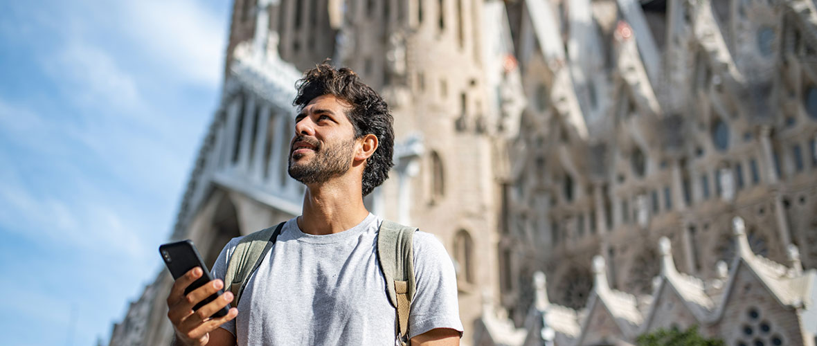 A 30 year old Hispanic male uses his smart phone in front of the Sagrada Familia in Barcelona, Spain in background.