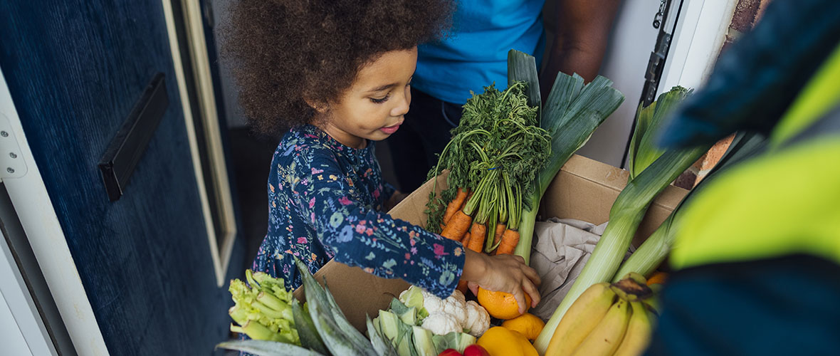 Small child receiving box of fresh vegetables