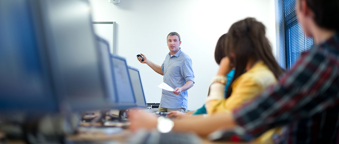 A teacher and his students, sitting among rows of computers