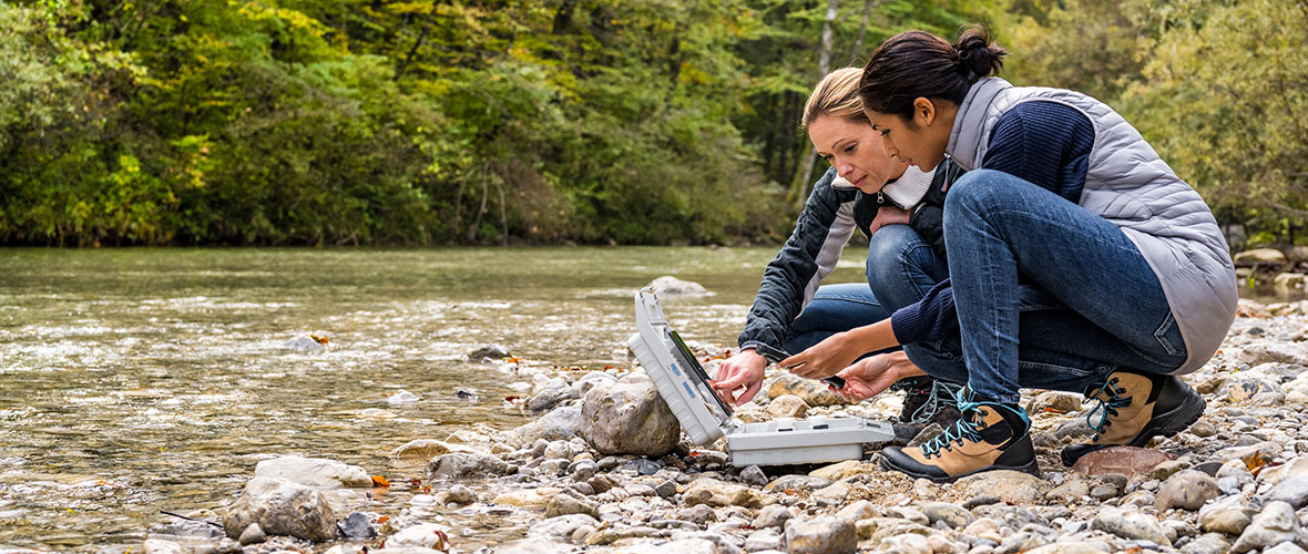 Biological researchers squatting at riverside and discussing measured data