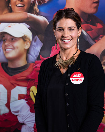 Ashley Martin Cockrell stands in front of the mural in the JSU Stadium that includes an image of her just after she kicked the field goal that made her the first female to suit up and score in a college football game.