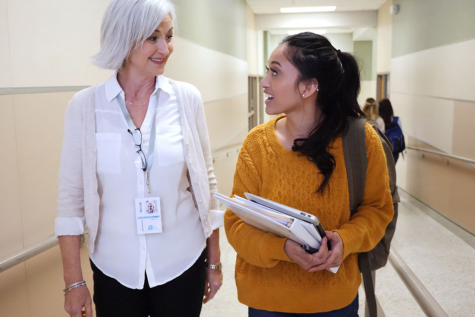 A principal and a student teacher walk and talk in the school hallway