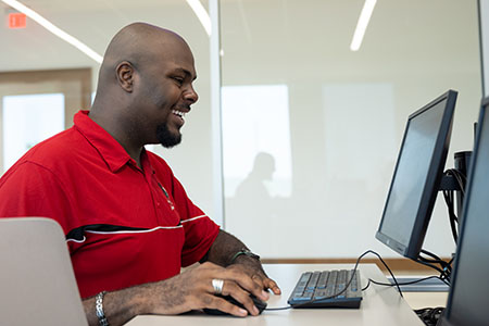 A male student sitting at a computer browsing scholarships 