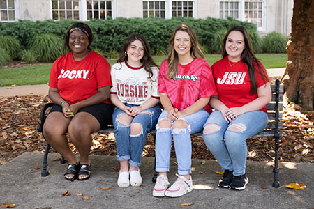 four students sitting on a bench on the quad