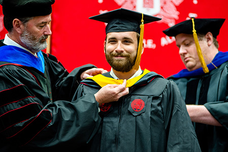 a  male graduate receives his hood at graduation