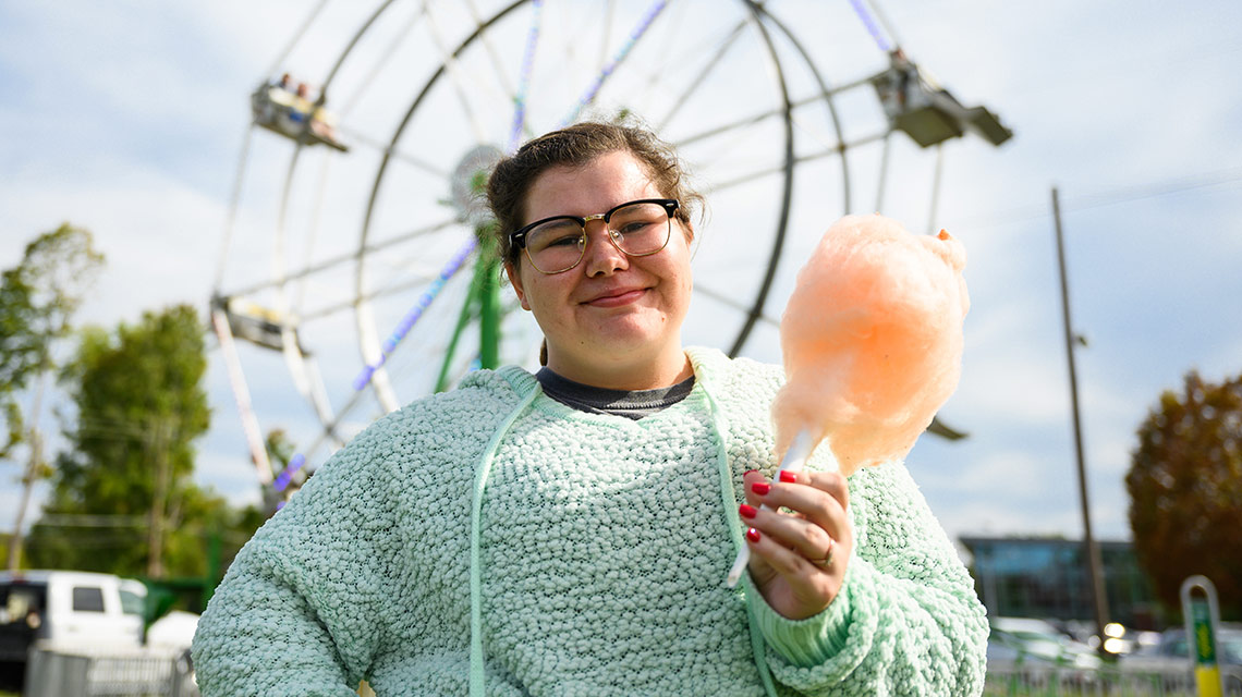 A student enjoys cotton candy in front of the ferris wheel at the Homecoming Carnival