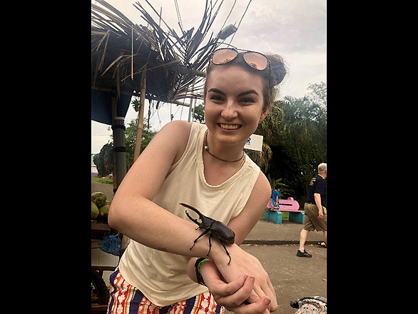 Honors student, Tara Maynard, holding a rhinoceros beetle while waiting for coconut water.