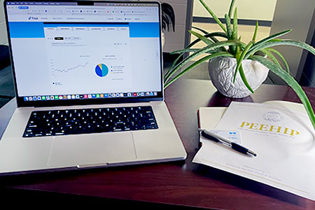 a computer open to the TIAA website, a copy of a PEEHIP insurance booklet and a BCBS insurance card lie on the desk of a JSU employee