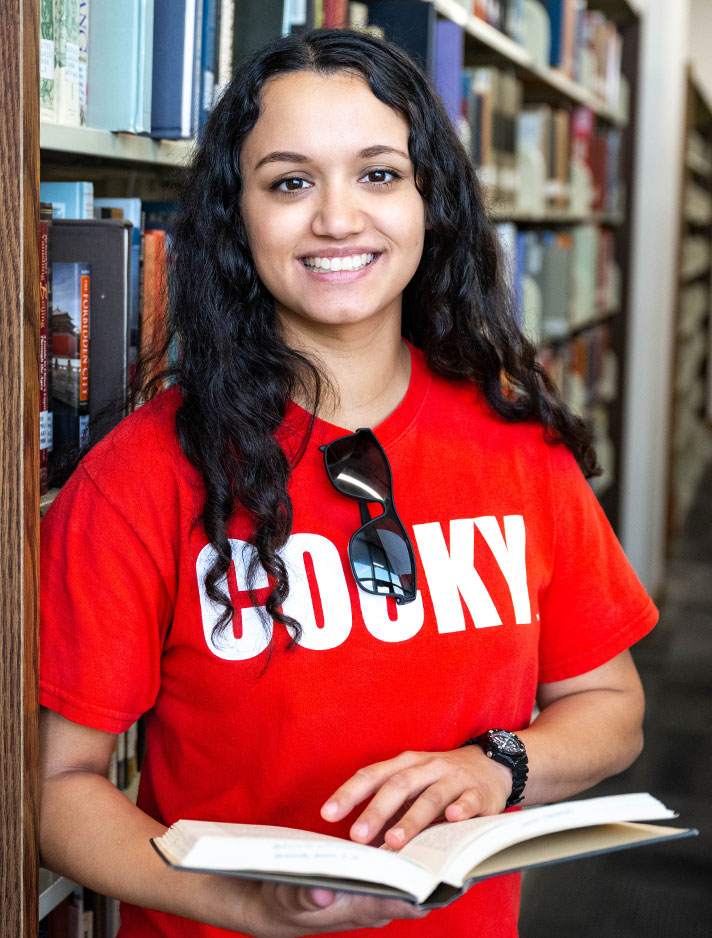 A female student, wearing her COCKY t-shirt, reads a book in the stacks at the Houston Cole Library