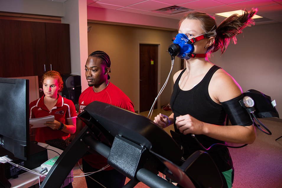 Students analyzing data while female runs on treadmill with oxygen monitoring mask