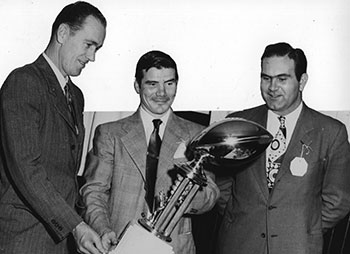 Members of the Jacksonville State College 1949-1950 Gamecock football coaching staff stand admiring their second Paper Bowl trophy. The first Paper Bowl trophy was won in 1948 in a game against Troy and the second Paper Bowl trophy was won in 1949 in the game against Livingston. Shown left to right are Ray Wedgeworth (line coach), Don Salls (head coach), and Tom Roberson (assistant coach).