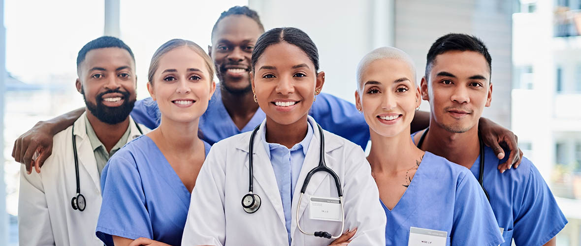 Three female nurses and a male nurse wearing a stethoscope stand outside an emergency room entrance.