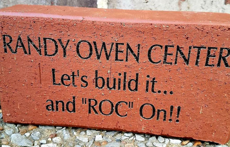 A Randy Owen Center brick engraved with the center's name and the phrase let's build it and roc on