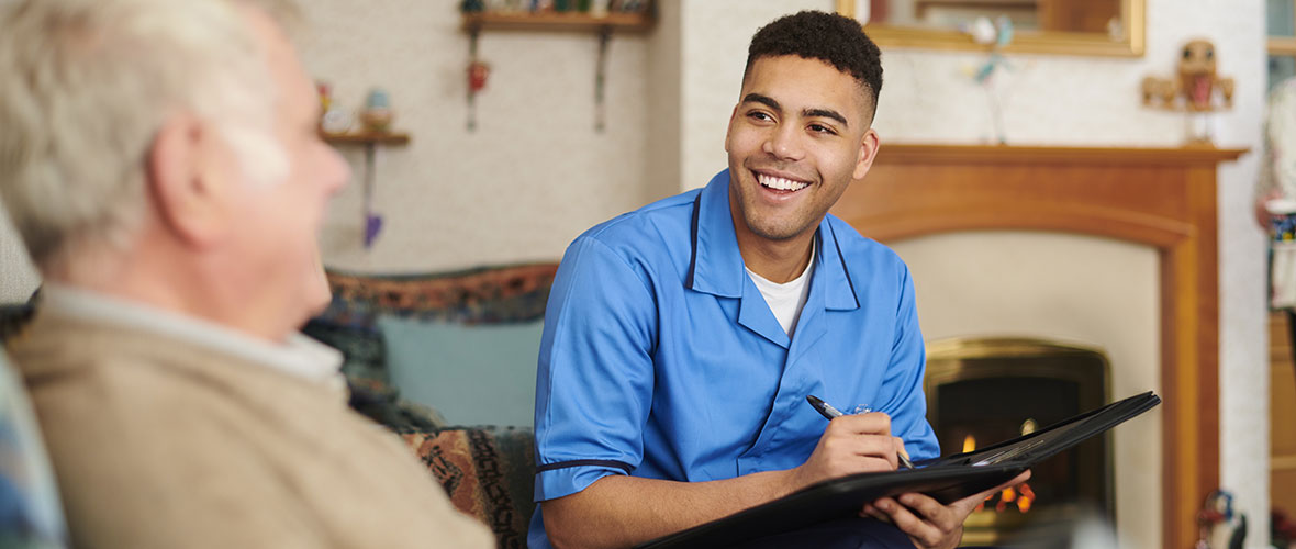 A male social worker takes notes during a visit in an elderly couple's home