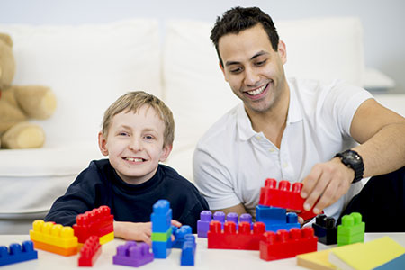 A social work student plays with blocks with a special needs student.