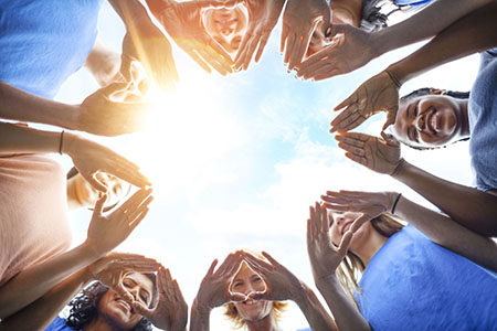 Young people stand in a circle, with their hands together to form hearts