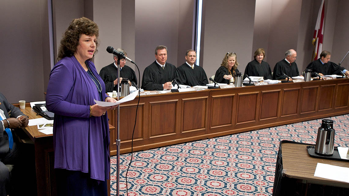 Dr. Lori Owen speaks to audience with the Alabama Supreme Court seated in the background.