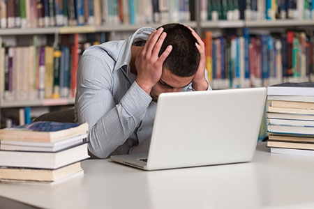Student holding head while looking at laptop