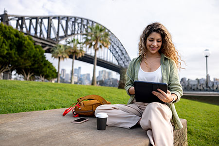 Female student on grass in front of bridge