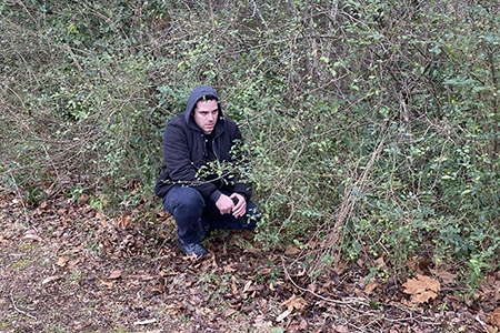 A man crouches in the woods