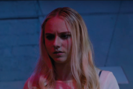A young woman stares off into the distance in a dark room