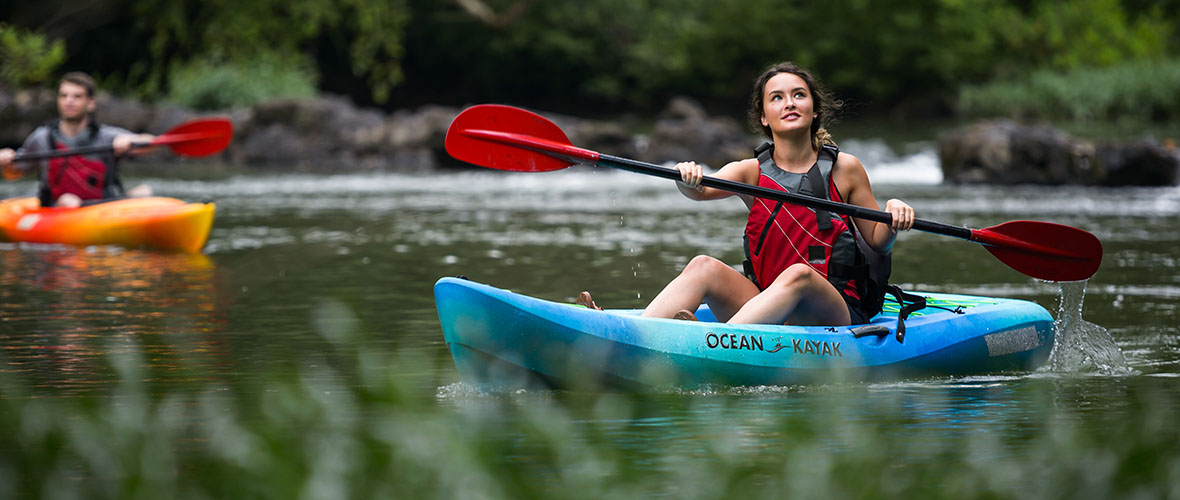 Female student looks up as she paddles on a river in a kayak.