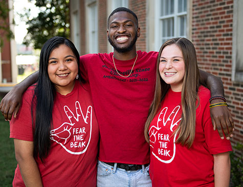Three smiling JSU students wearing JSU tees embrace on the Quad
