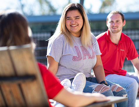 A smiling female student visits with fellow students on the patio at the Rec Center